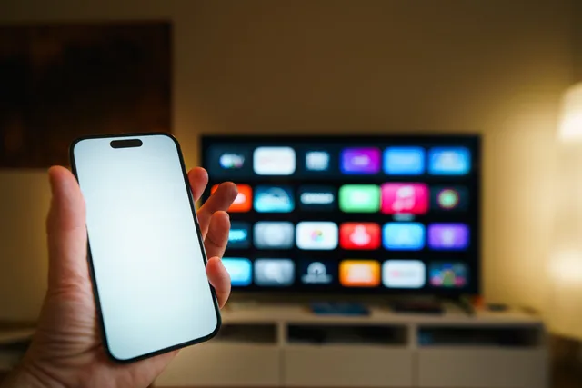 A smartphone in focus with a smart TV displaying apps in a cozy living room. 2 questions to ask before a Belfast connected TV campaign