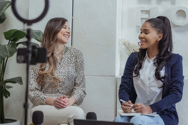 Two women engaged in a lively conversation in a professional interview setting. Connected TV advertising customer interviews: a six-step checklist and scoring rubric