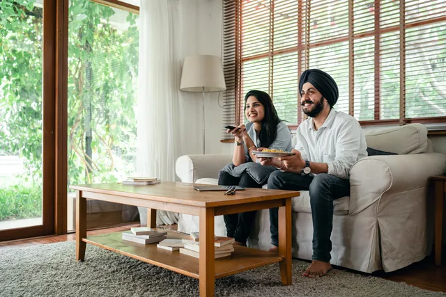 Cheerful Indian woman and man in turban spending free time together while watching television and sitting on sofa in living room near table. How to score Connected TV advertising platforms
