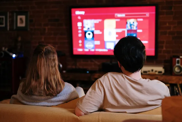 A couple enjoys streaming shows on a large TV in a cozy, brick-walled living room. Check connected TV advertising service standards before you sign