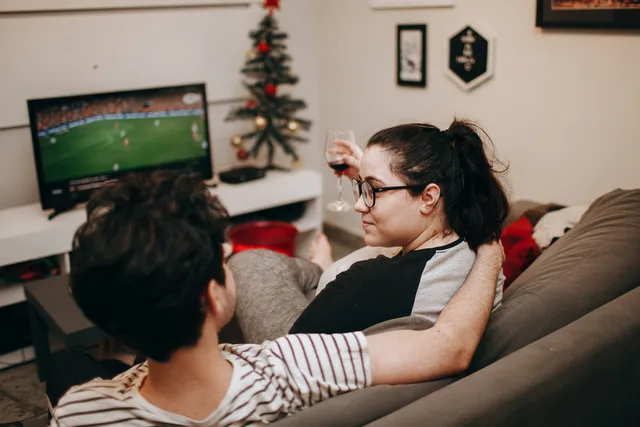 A couple enjoying a cozy evening on the sofa, watching TV with holiday decor in the background. Check these connected TV advertising tools and providers before you commit budget