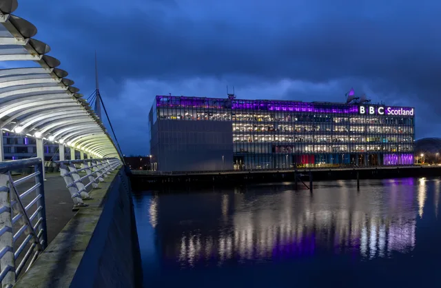 Night view of the BBC Scotland building with purple lights reflecting on the River Clyde in Glasgow. Streaming ads in Wales and Scotland: language and access